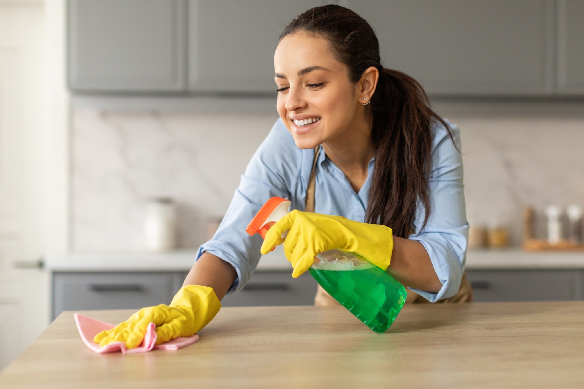 cheerful,young,woman,wearing,yellow,gloves,and,blue,shirt,cleans